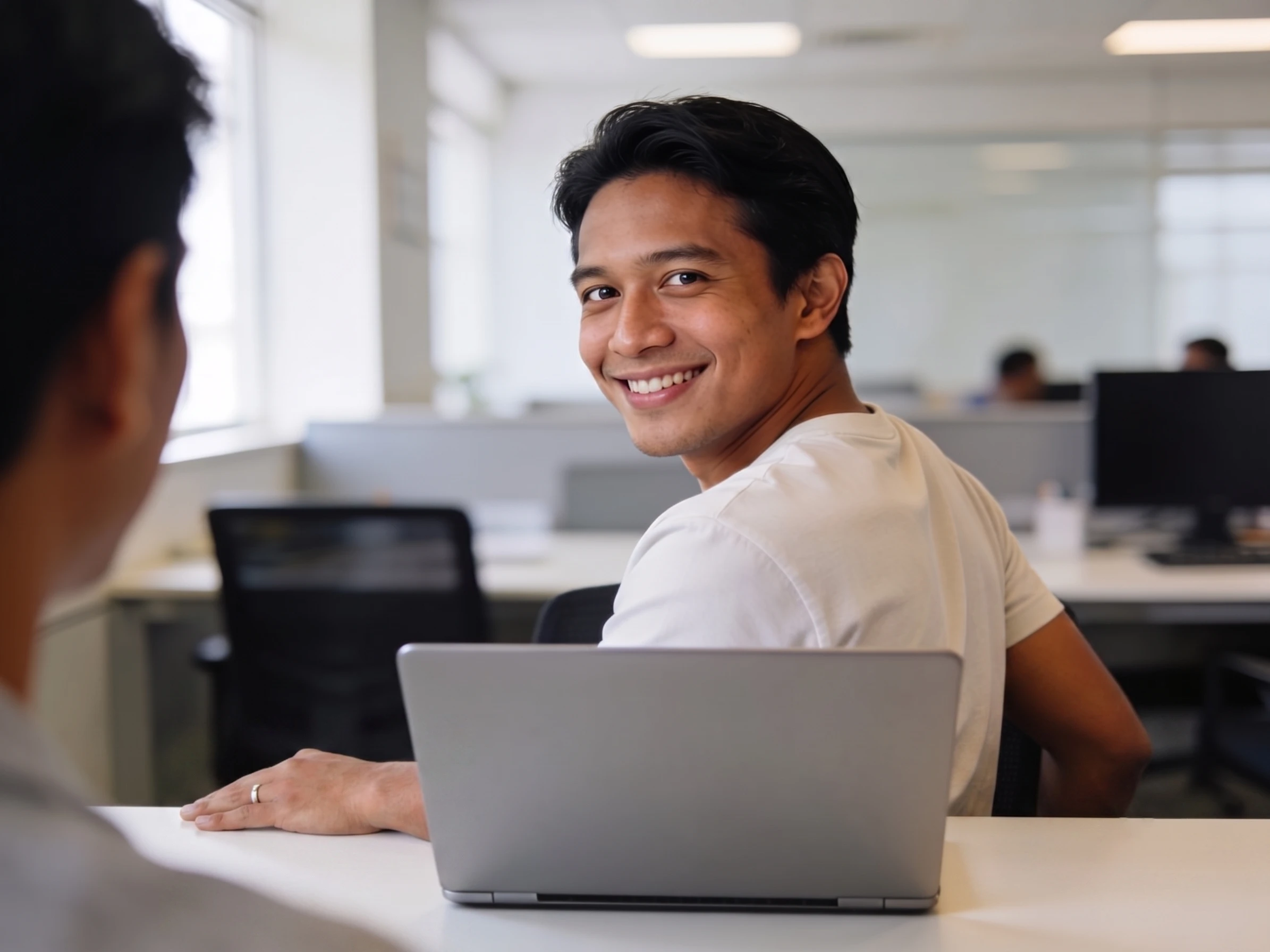Pria Indonesia profesional tersenyum natural berdiskusi dengan rekan kerja di kantor modern.